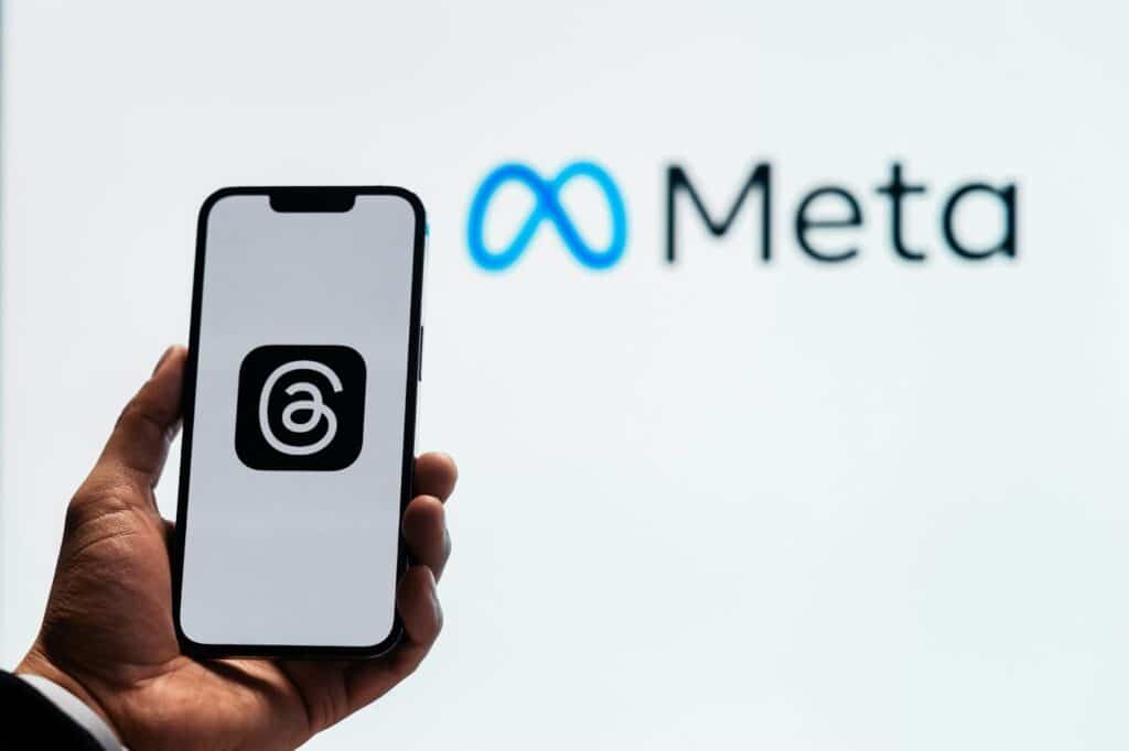Pessoa segurando um smartphone com o logótipo da aplicação Threads da Meta, com o logótipo da Meta desfocado ao fundo.